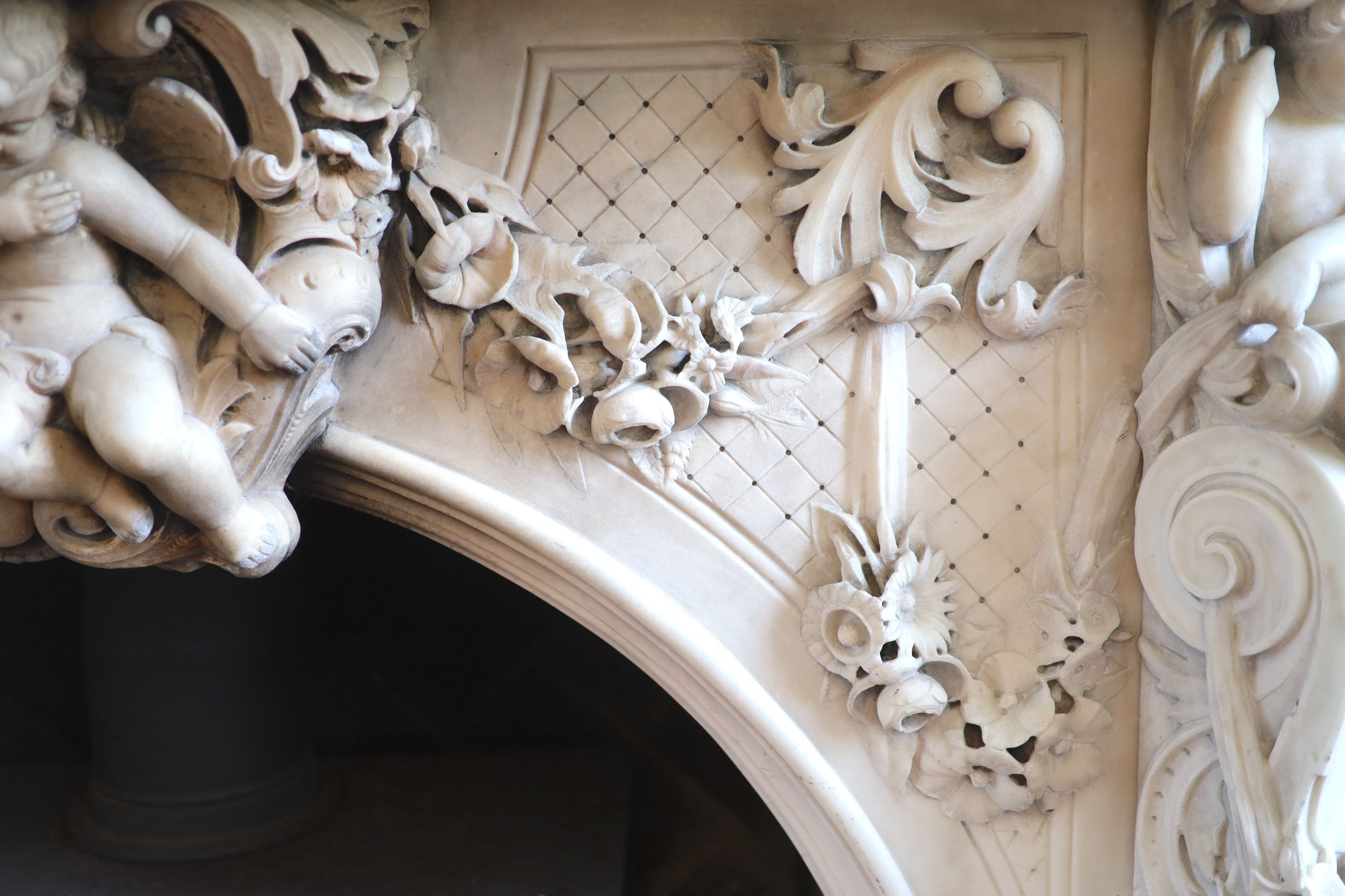 An important mid 19th century Italian white Carrara marble chimney piece, carved in the rococo taste, with seated putti, foliage swags